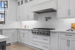Gourmet kitchen featuring a stainless steel range, white shaker cabinetry, stone countertops, a pot filler, and light wood-finish flooring - 