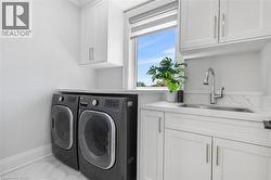 Dedicated laundry area featuring white shaker cabinetry, an integrated stainless steel sink, a modern pull-down faucet, a white countertop, and large format marble-look floor tiling - 