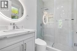 Contemporary bathroom featuring a floating white vanity with a marble-finish countertop, an illuminated round mirror, and a glass-enclosed shower with a rainfall showerhead - 