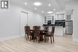 Open-concept recreation room featuring light wood-finish flooring, recessed lighting, and a built-in wet bar with white cabinetry, a black and white veined countertop, and a stainless steel refrigerat - 