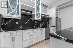 Contemporary kitchen featuring white cabinetry with silver hardware, contrasting dark countertops and backsplash with prominent white veining, a stainless steel dishwasher, and a built-in wine rack - 