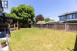Expansive backyard featuring a manicured lawn, a full wooden fence, and a covered wooden deck with stairs - 