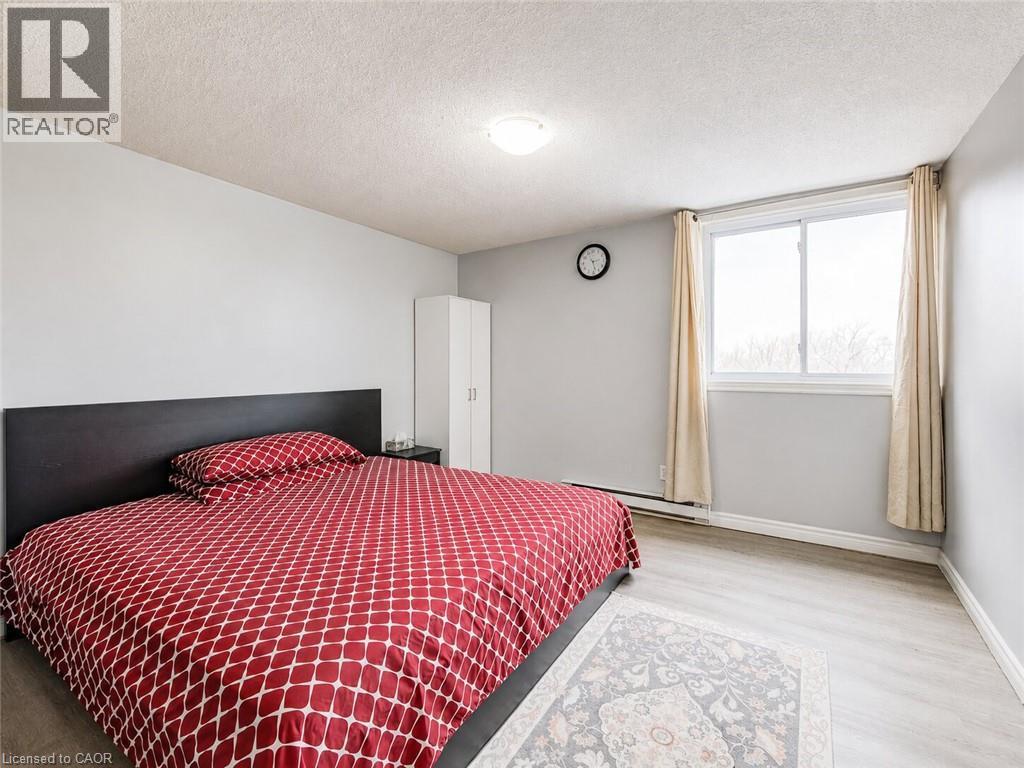 Bright bedroom with light gray walls, wood-finish flooring, a white wardrobe, and a large window with drapes - 4 Avalon Place Unit# 303, Kitchener, ON