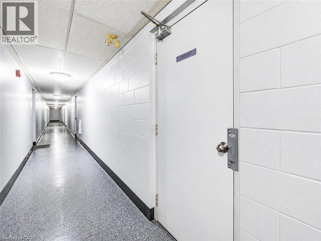 Long hallway with durable block walls, tile ceiling, and speckled flooring - 4 Avalon Place Unit# 303, Kitchener, ON