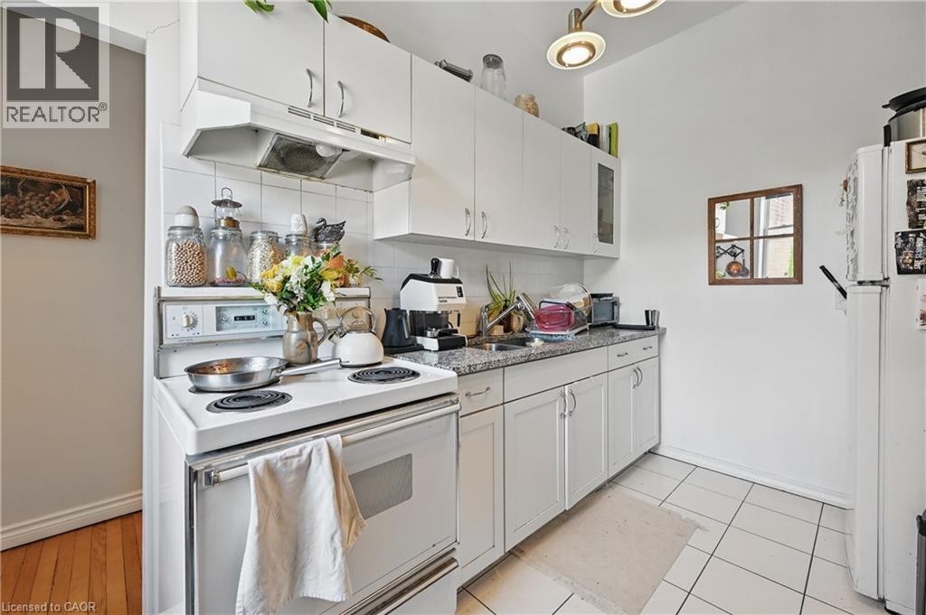 White cabinetry, stone-finish countertop, white tile flooring, and a white range with overhead ventilation - 55 Barton Street W, Hamilton, ON