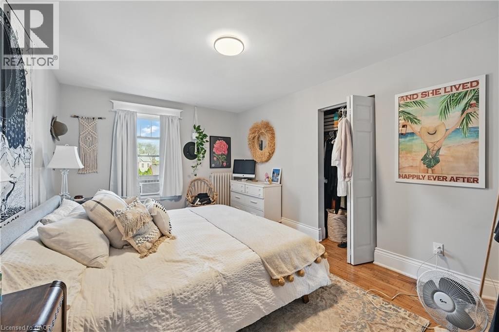 Hardwood flooring, white painted walls, window with trim, bi-fold closet door, and overhead flush-mount lighting - 55 Barton Street W, Hamilton, ON