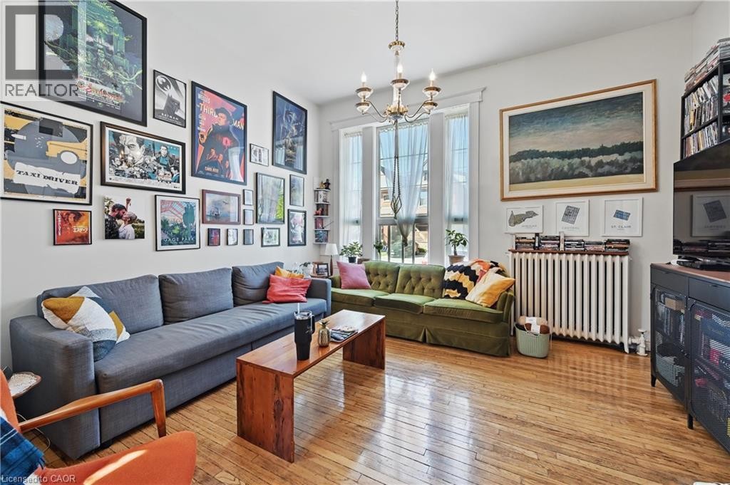 Hardwood flooring, prominent windows with natural light, a chandelier, a wall-mounted radiator, and an entertainment console - 55 Barton Street W, Hamilton, ON