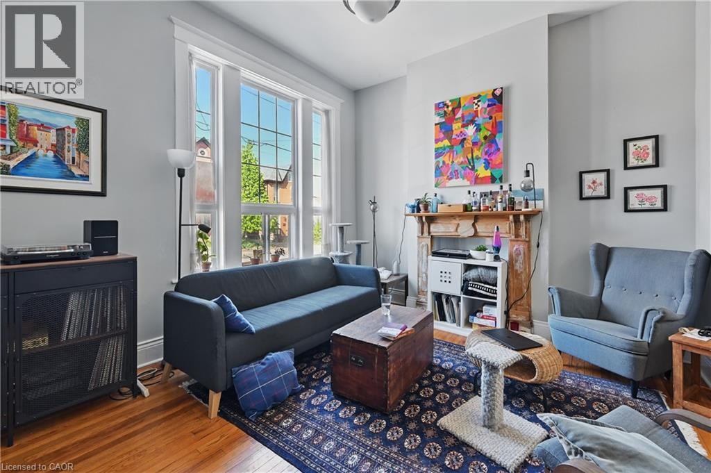 Hardwood flooring, multi-pane windows with white trim, a decorative fireplace with a wood mantel, and light gray wall finishes - 55 Barton Street W, Hamilton, ON