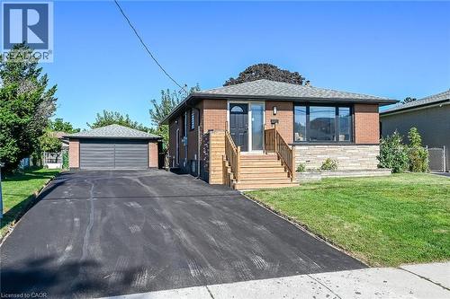 Brick exterior with stone accents, wood staircase, large picture window, attached garage, and paved driveway - 135 Nugent Drive, Hamilton, ON 
