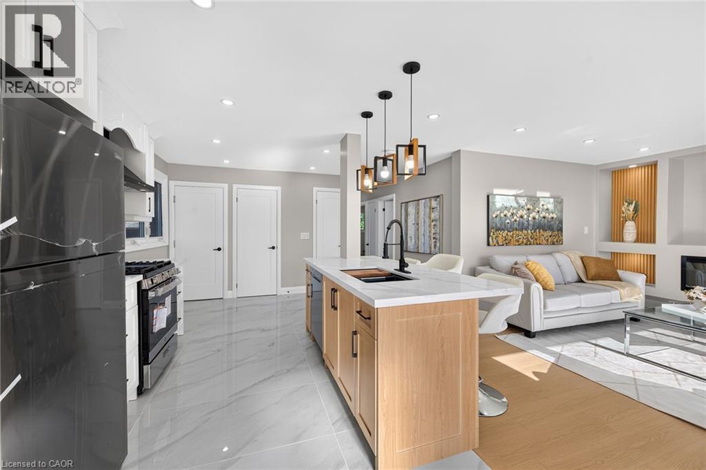 Kitchen island with a white countertop and integrated sink, pendant lighting, stainless steel appliances, and tile flooring - 135 Nugent Drive, Hamilton, ON