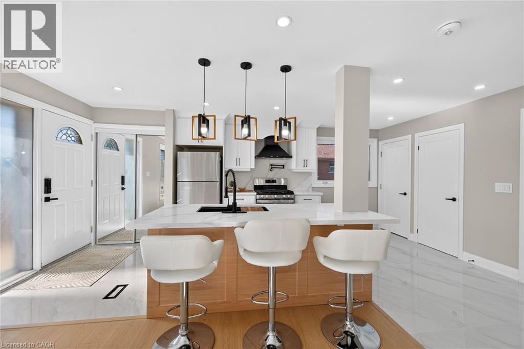 Open-concept kitchen featuring an island with a light wood finish, white countertop, and stainless steel appliances - 135 Nugent Drive, Hamilton, ON