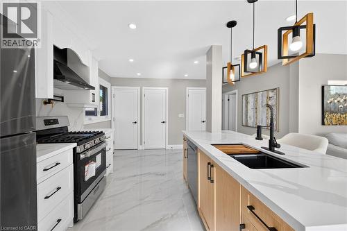 Modern kitchen featuring white shaker cabinetry, stainless steel appliances, a large center island with a black sink, and pendant lighting - 135 Nugent Drive, Hamilton, ON 