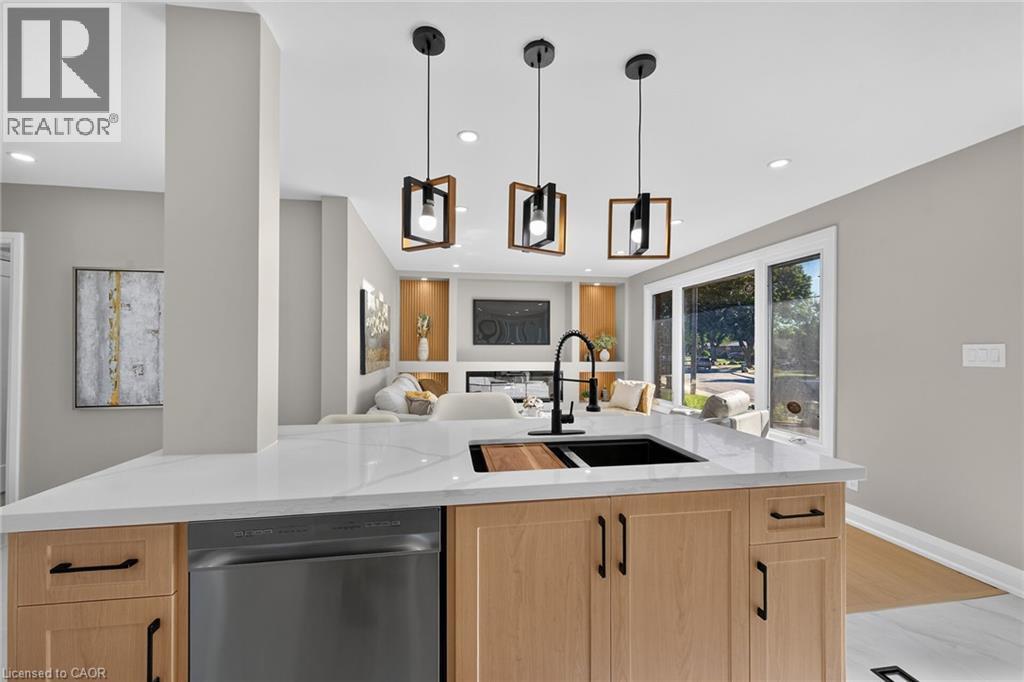 Kitchen island featuring a white countertop, undermount sink with a matte black faucet, and light wood-finish cabinetry with black hardware - 135 Nugent Drive, Hamilton, ON