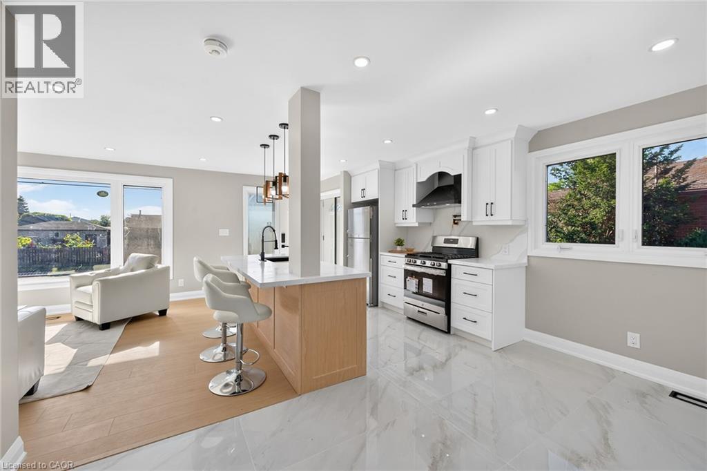 Bright, open-concept living space featuring a kitchen island with pendant lighting, stainless steel appliances, white cabinetry, and large windows - 135 Nugent Drive, Hamilton, ON
