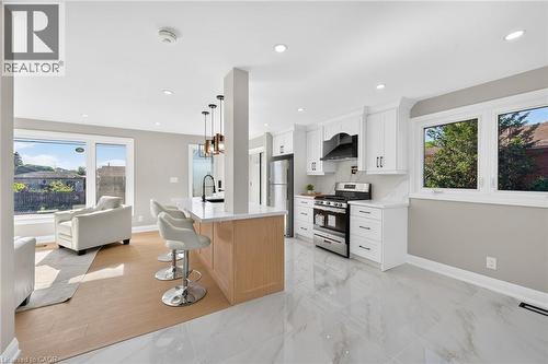 Bright, open-concept living space featuring a kitchen island with pendant lighting, stainless steel appliances, white cabinetry, and large windows - 135 Nugent Drive, Hamilton, ON 