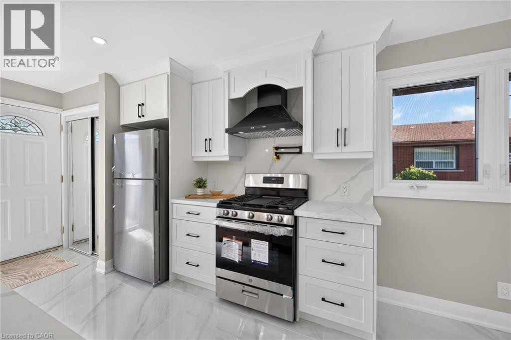 Kitchen with white cabinetry, stainless steel appliances, solid surface countertops, a gas range, and a decorative range hood - 135 Nugent Drive, Hamilton, ON