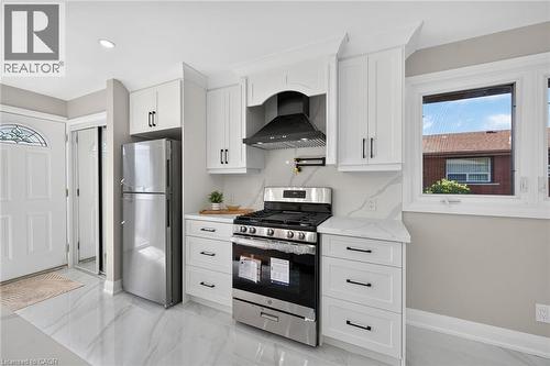 Kitchen with white cabinetry, stainless steel appliances, solid surface countertops, a gas range, and a decorative range hood - 135 Nugent Drive, Hamilton, ON 