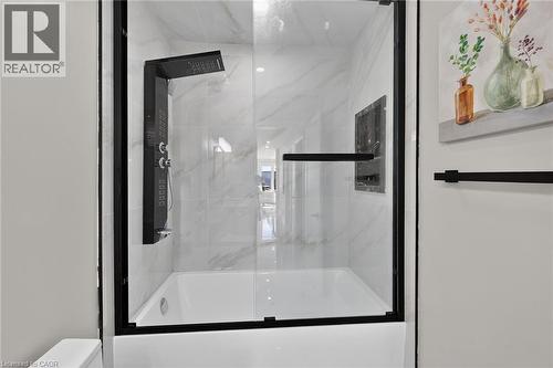Modern shower enclosure featuring frameless glass panels with black metal hardware, a linear showerhead, and a spacious white base - 135 Nugent Drive, Hamilton, ON 