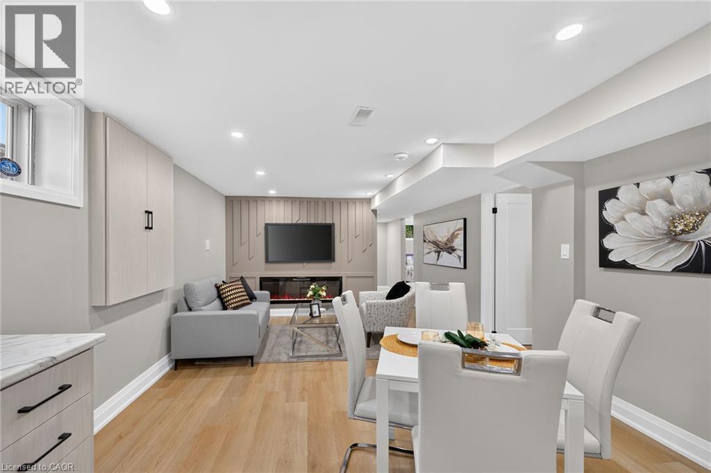 Recessed lighting, wood-finish flooring, built-in wall cabinetry, built-in electric fireplace, and a dining area with a white table - 135 Nugent Drive, Hamilton, ON