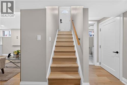 Hardwood staircase with natural wood handrail, light gray wall finishes, white interior doors with matte black hardware, and wood-finish flooring - 135 Nugent Drive, Hamilton, ON 