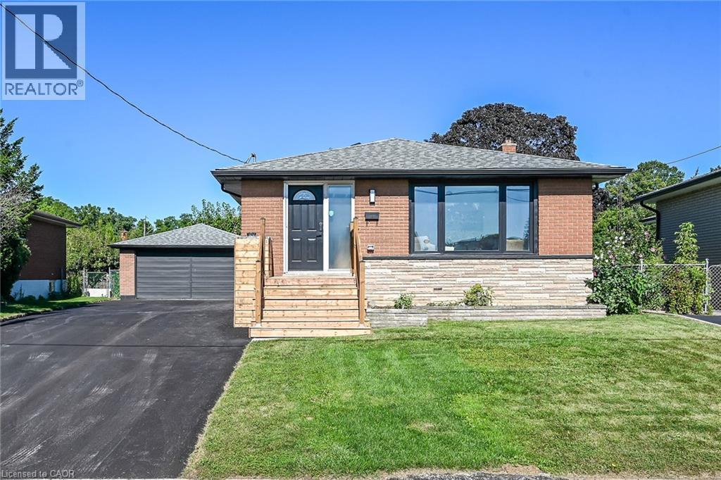 Brick facade with stone detailing, large picture window, new wood-finish entry steps, asphalt driveway, and detached garage - 135 Nugent Drive, Hamilton, ON