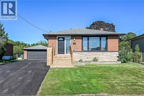 Brick facade with stone detailing, large picture window, new wood-finish entry steps, asphalt driveway, and detached garage - 135 Nugent Drive, Hamilton, ON 
