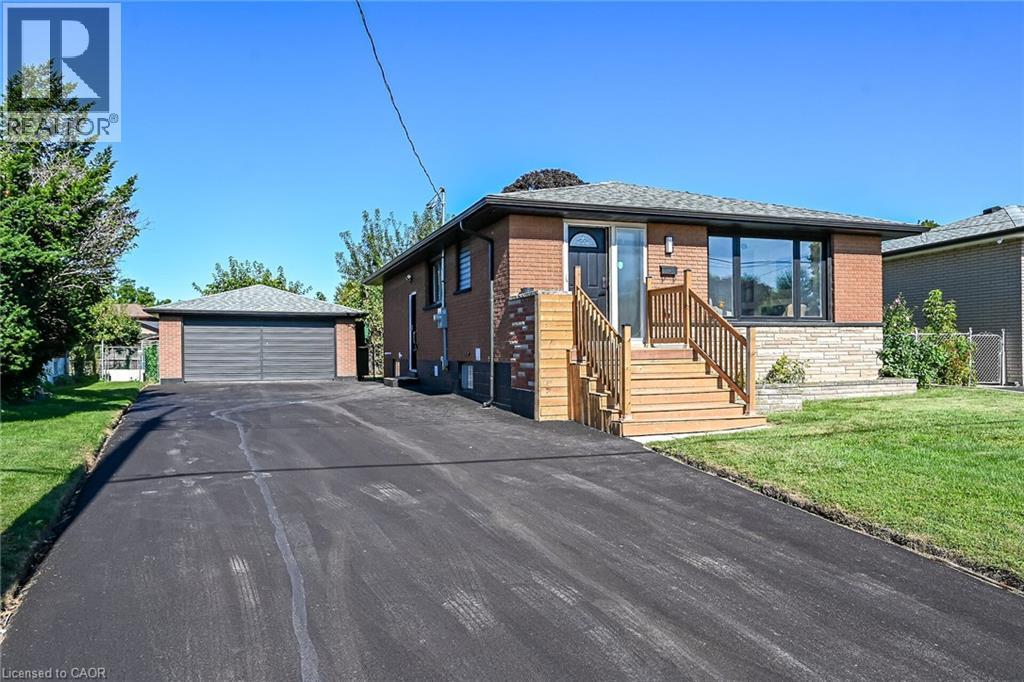 Brick exterior with stone accents, wood staircase with railing, front entry door with transom window, expansive paved driveway, and detached two-car garage - 135 Nugent Drive, Hamilton, ON