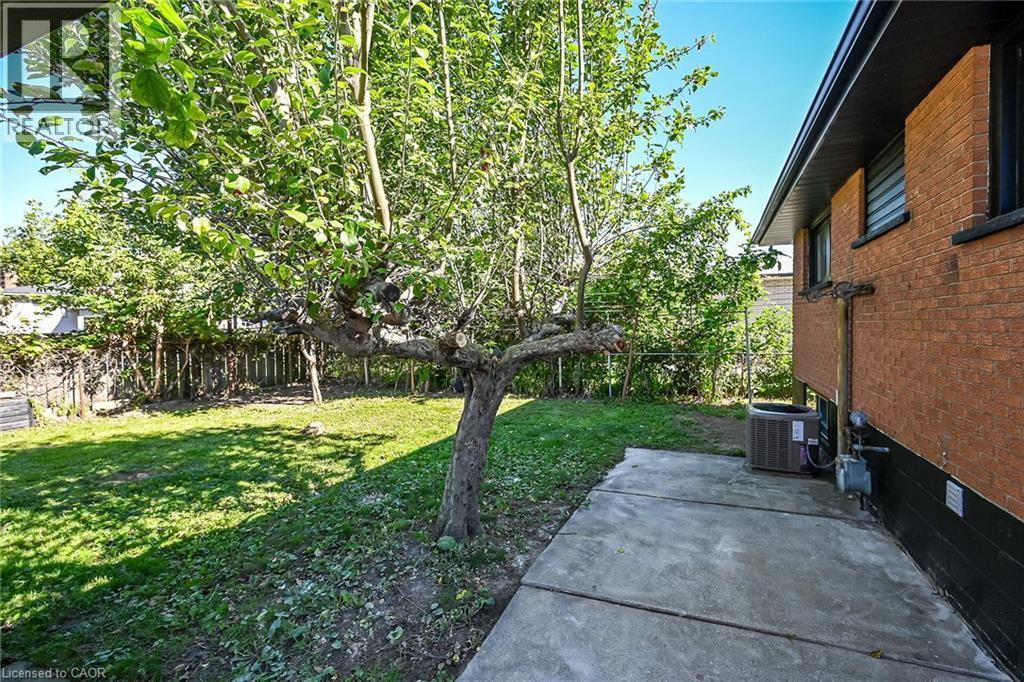 Expansive rear yard featuring a concrete patio, mature tree, and red brick exterior - 135 Nugent Drive, Hamilton, ON