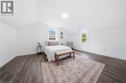 Spacious primary bedroom featuring wood-finish flooring, recessed ceiling lighting, and multiple windows providing natural illumination - 