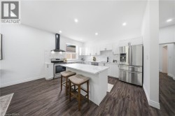 Modern kitchen featuring wood-finish flooring, white cabinetry, stainless steel appliances, a white subway tile backsplash, and an island with a light-toned countertop - 