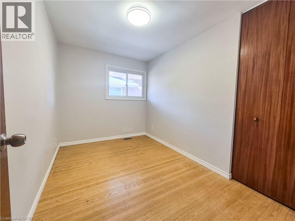 Hardwood flooring, wood-finish closet door, white walls, flush mount ceiling light, and a white window frame - 11 Duncairn Avenue, Kitchener, ON