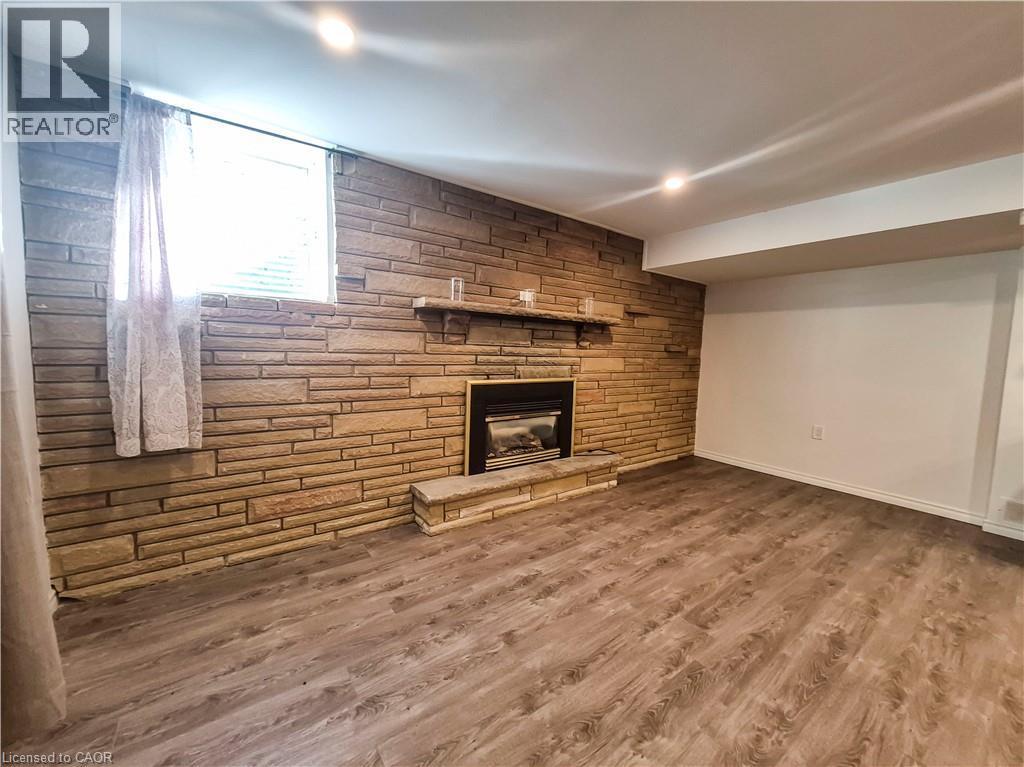 Stone accent wall featuring a built-in fireplace, wood-finish flooring, recessed lighting, and a window with blinds - 11 Duncairn Avenue, Kitchener, ON