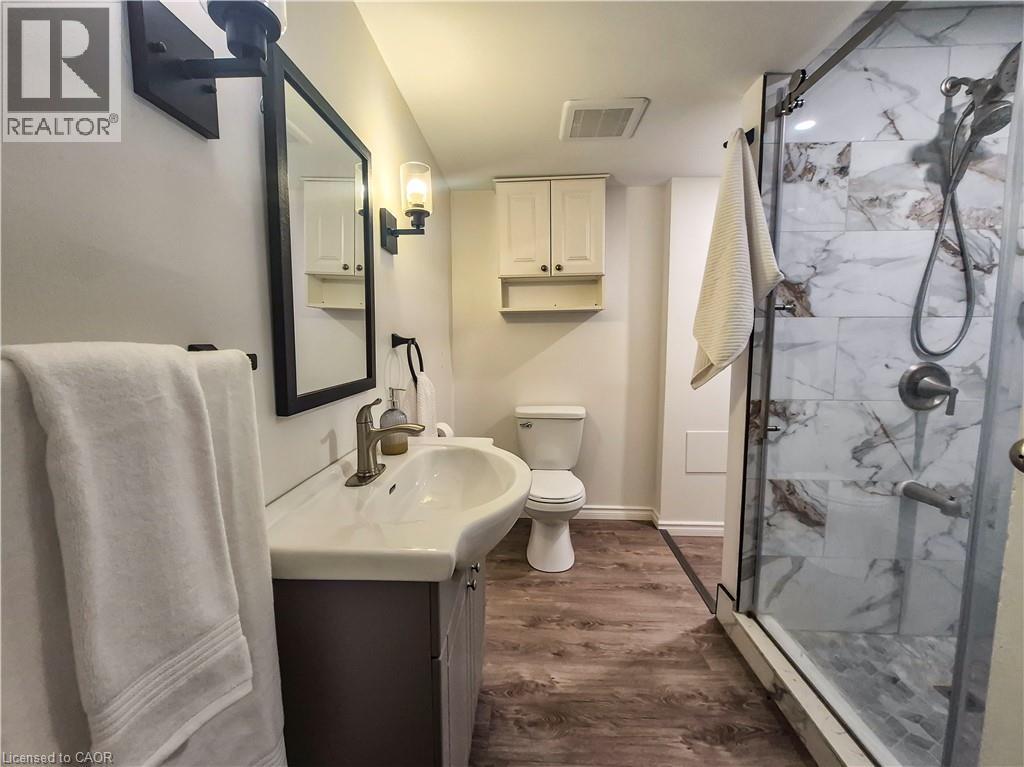 Glass-enclosed shower with tiled walls and floor, vanity with an integrated sink, wood-finish flooring, and wall-mounted lighting fixtures - 11 Duncairn Avenue, Kitchener, ON