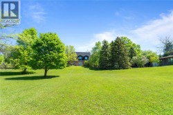 Expansive green lawn with mature trees and a distant brick-clad residence featuring dormer windows - 
