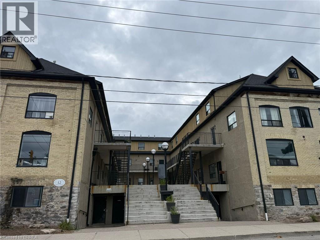 Brick and stone facade building with multiple windows, black roof, and exterior stairways - 12 Bridgeport Road E Unit# 18, Waterloo, ON