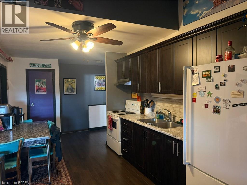Kitchen featuring wood-finish flooring, dark wood cabinetry, light-toned countertops, tile backsplash, and a ceiling fan with integrated lighting - 12 Bridgeport Road E Unit# 18, Waterloo, ON