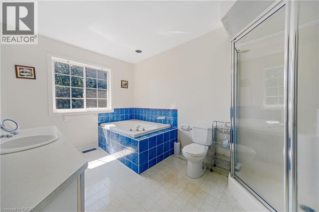 Jetted soaking tub with blue tile surround, white vanity with integrated sink, glass-enclosed shower, and a white grid-pane window - 82 Milner Downs Crescent, Ottawa, ON