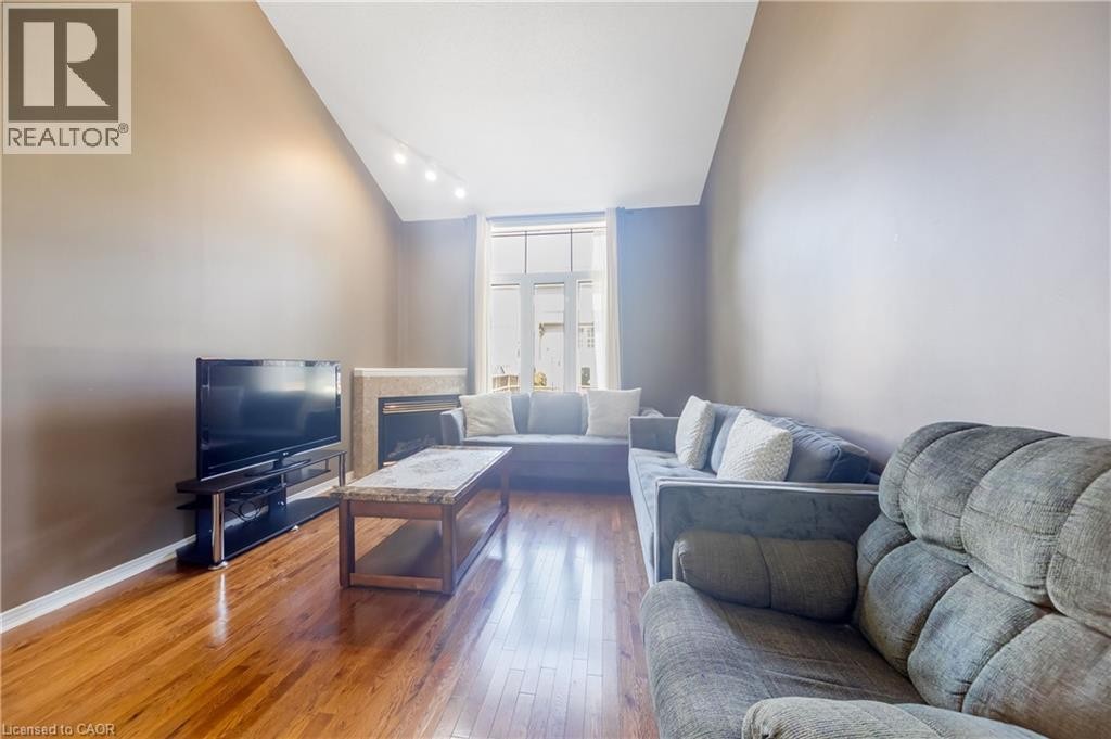 Vaulted ceiling with track lighting, fireplace with stone surround, large window, and wood-finish flooring - 82 Milner Downs Crescent, Ottawa, ON