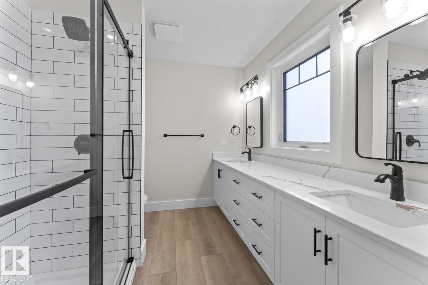 This bathroom features a double vanity with white cabinetry, black hardware, and white countertops - 807 Schooner Drive, Cold Lake, AB - Indoor Photo Showing Bathroom