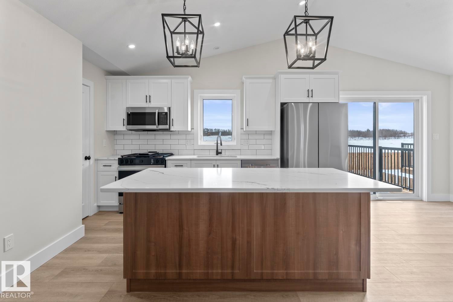 The kitchen features a spacious island with a white countertop and wood paneling, white cabinetry, stainless steel appliances, and a white subway tile backsplash - 807 Schooner Drive, Cold Lake, AB - Indoor Photo Showing Kitchen With Upgraded Kitchen