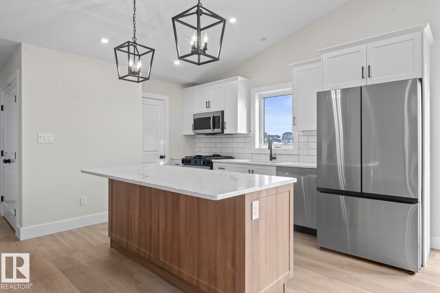 The kitchen features a central island with a light wood finish and a white countertop, complemented by white cabinetry and stainless steel appliances, including a microwave, oven, and refrigerator - 807 Schooner Drive, Cold Lake, AB - Indoor Photo Showing Kitchen With Stainless Steel Kitchen With Upgraded Kitchen