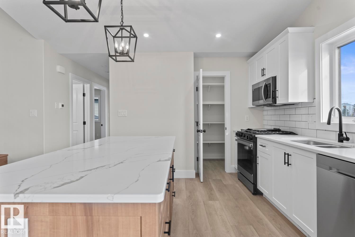 The kitchen features a spacious island with a marble-effect countertop, white cabinetry with black hardware, and a stainless steel dishwasher - 807 Schooner Drive, Cold Lake, AB - Indoor Photo Showing Kitchen With Double Sink With Upgraded Kitchen