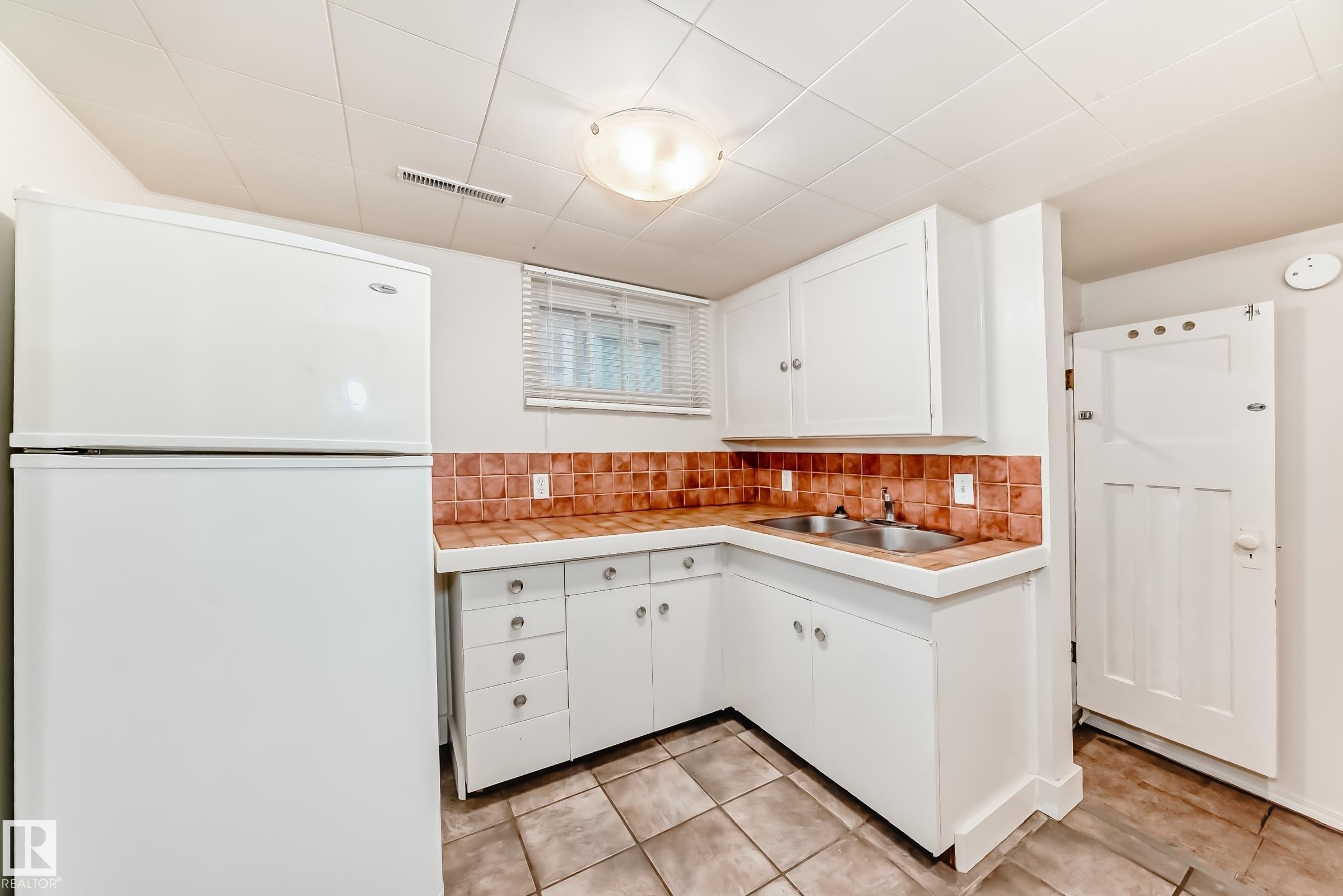 Kitchen with freestanding refrigerator, tile countertops, white cabinets, and decorative backsplash - 12605 107 Avenue, Edmonton, AB - Indoor Photo Showing Kitchen With Double Sink