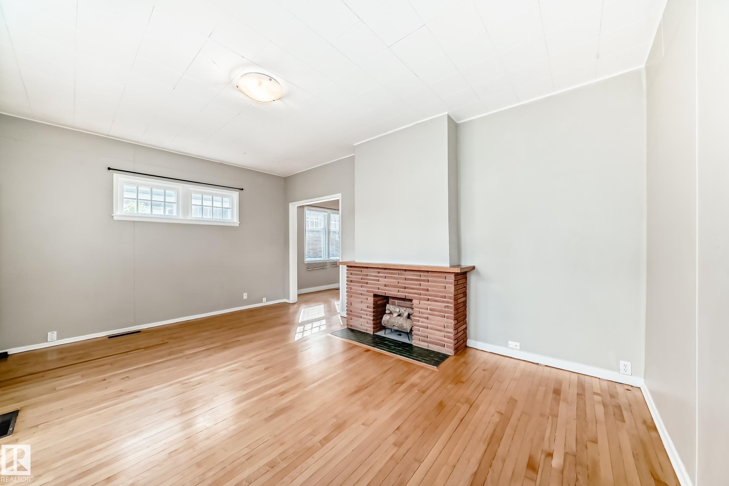 Unfurnished living room featuring hardwood / wood-style floors and a brick fireplace - 12605 107 Avenue, Edmonton, AB - Indoor With Fireplace
