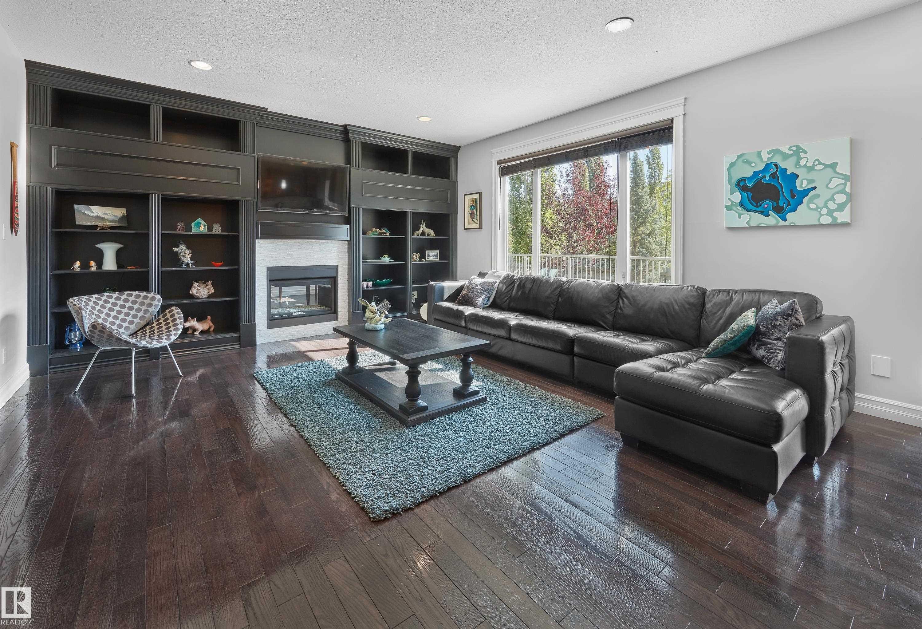 Living area featuring a textured ceiling, dark wood-style flooring, a glass covered fireplace, recessed lighting, and built in features - 4111 Westcliff Heath Heath, Edmonton, AB - Indoor Photo Showing Living Room With Fireplace
