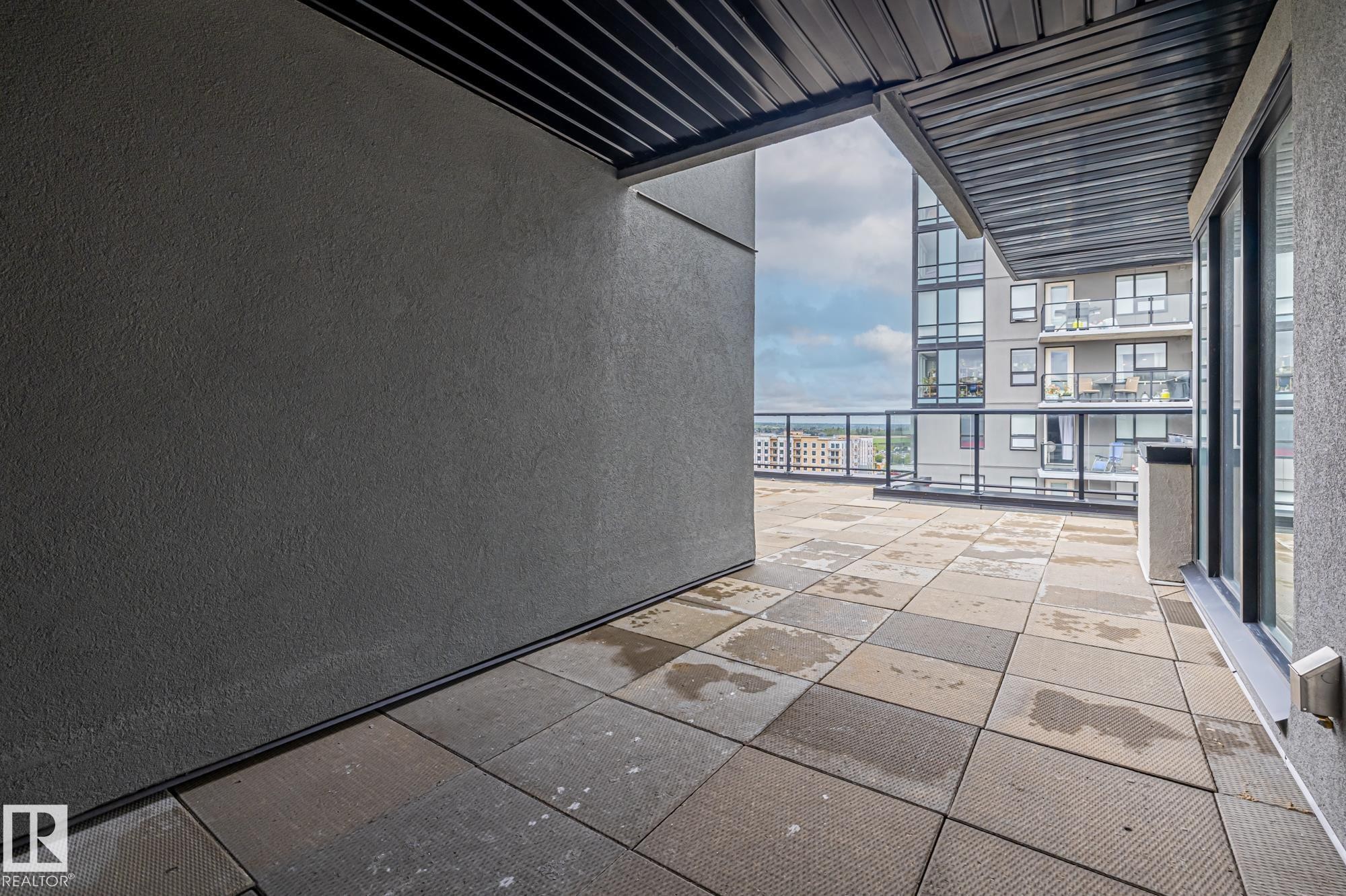 Empty room with a textured wall, floor to ceiling windows, and stone tile flooring - 810 5151 Windermere Boulevard, Edmonton, AB - Outdoor