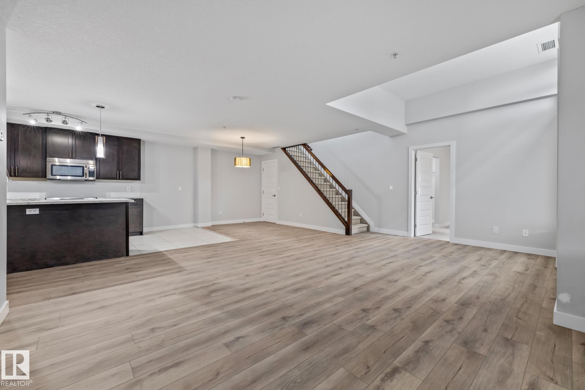 Unfurnished living room with light wood-type flooring and stairs - 810 5151 Windermere Boulevard, Edmonton, AB - Indoor Photo Showing Other Room