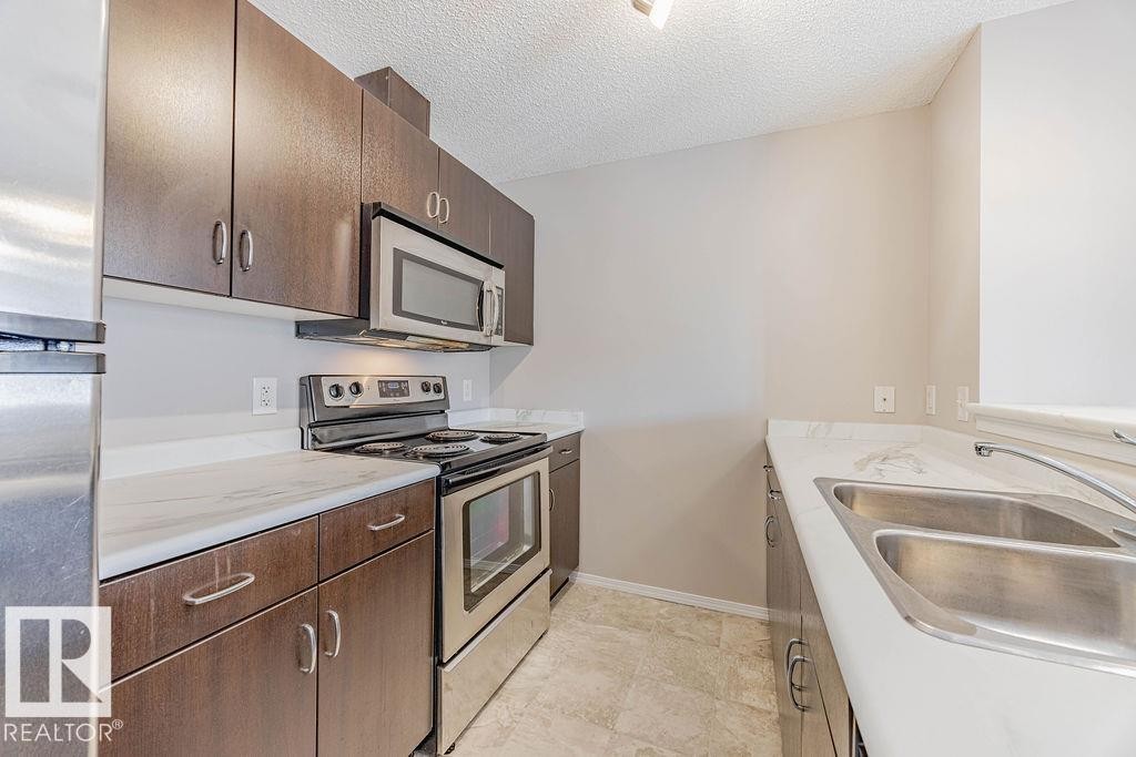 Kitchen featuring stainless steel appliances, a textured ceiling, light countertops, dark brown cabinetry, and light tile patterned flooring - Edmonton, AB - Indoor Photo Showing Kitchen With Double Sink