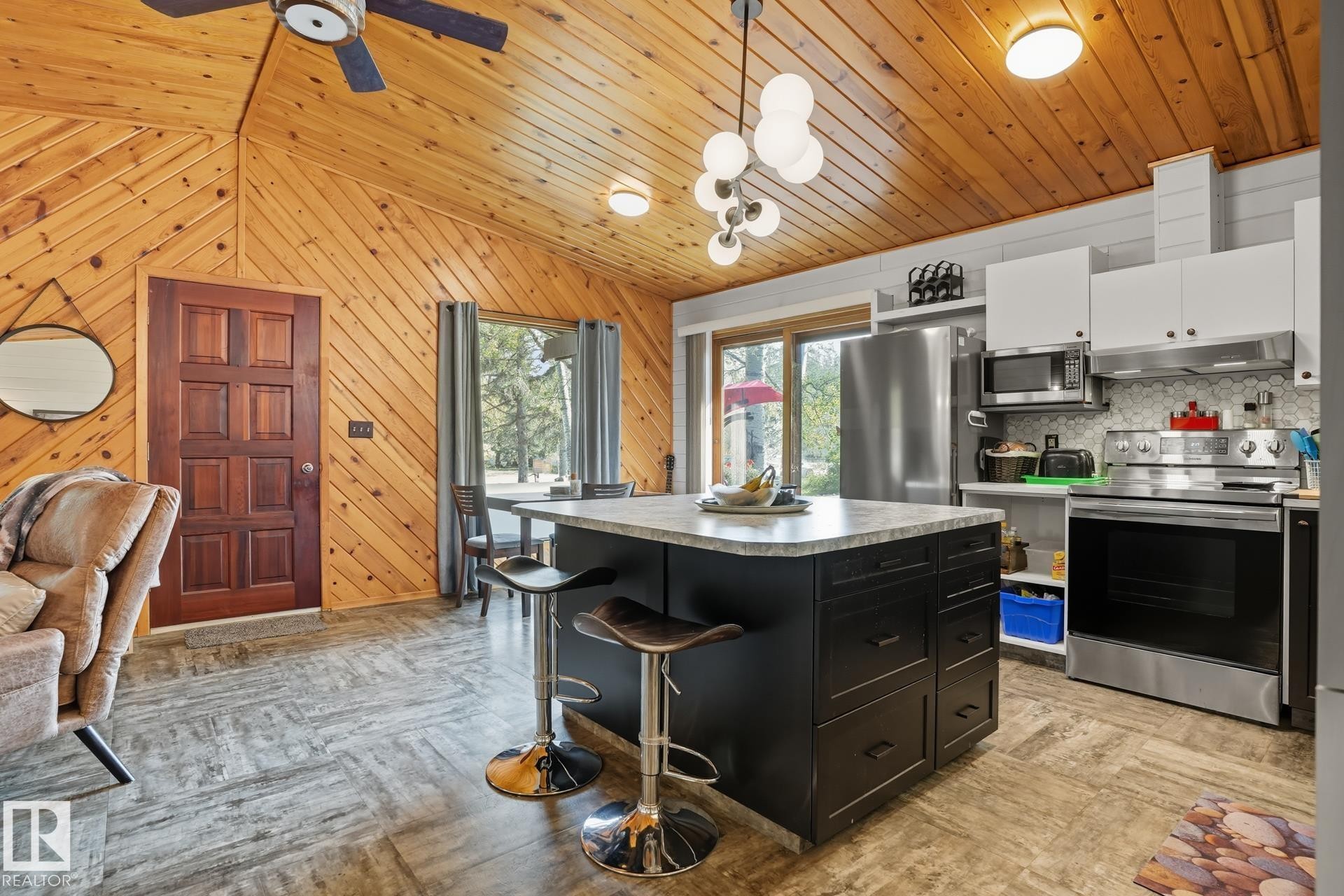 Kitchen with a kitchen breakfast bar, appliances with stainless steel finishes, dark cabinetry, pendant lighting, and wood walls - 6309 49 St, Rural Wetaskiwin County, AB - Indoor Photo Showing Kitchen
