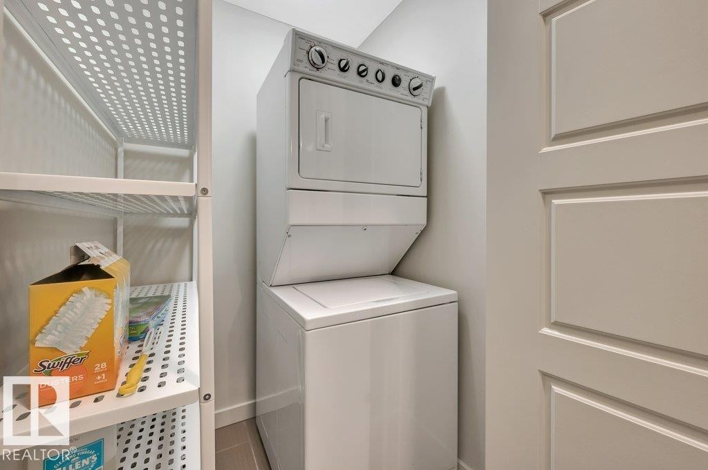 Laundry area featuring stacked washer / dryer and baseboards - 140 308 Ambleside Link, Edmonton, AB - Indoor Photo Showing Laundry Room